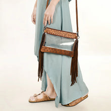 Load image into Gallery viewer, Brass Tacks Tan fringe clear crossbody held at the side, studded base and tooled band