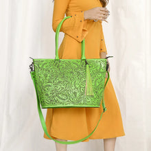 Load image into Gallery viewer, Model carrying the Maple Creek hand tooled leather tote in green by its rolled handles