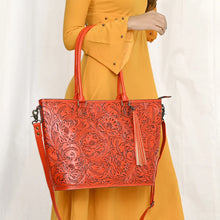 Load image into Gallery viewer, Model carrying the Maple Creek hand tooled leather tote in red on her forearm by its rolled handles