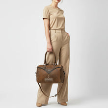 Load image into Gallery viewer, Model carrying the Bowie western satchel by its rolled leather handles, showing the bag's scale against the body with the crossbody strap hanging loose