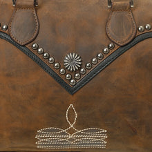 Load image into Gallery viewer, Close-up of the Bowie satchel's black leather V-yoke edged in gunmetal dome studs with a single starburst concho at the point, above the cream contrast sprig stitching