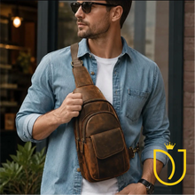 Load image into Gallery viewer, Drifter distressed brown leather sling bag worn crossbody over a denim shirt, showing the front flap pocket and brass hardware