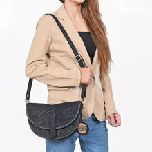 Load image into Gallery viewer, Woman wearing the Nightshade black embossed suede saddle crossbody over a blazer and jeans