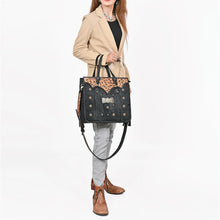 Load image into Gallery viewer, Woman carrying the Fandango black hair-on leather fringe tote by its braided handles, styled with a camel blazer, gray jeans, and tooled western boots