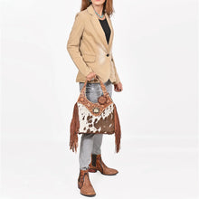 Load image into Gallery viewer, Model carrying the Appaloosa cowhide fringe hobo with a tan blazer, gray jeans and tooled boots