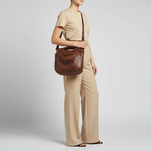 Load image into Gallery viewer, Model wearing the Selene brown studded leather crescent handbag on the shoulder with neutral wide-leg trousers
