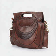 Load image into Gallery viewer, Angled view of the Selene brown leather handbag showing tonal smooth and pebbled crescent panels and studded clutch handle
