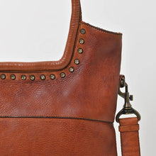 Load image into Gallery viewer, Close-up of Sienna tote in cognac showing antique brass star-head studs framing the rolled handle and a brass swivel strap clip
