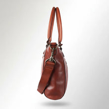 Load image into Gallery viewer, Side view of the Rowan cognac leather satchel showing its depth, rolled handles and brass swivel clip on the crossbody strap

