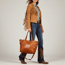 Load image into Gallery viewer, Model in a fringe suede jacket and cowboy boots carrying the Emmylou studded Italian leather tote in honey tan
