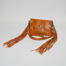 Load image into Gallery viewer, Angled view of the Estrella tan studded leather crossbody with fringe falling from both sides and the adjustable strap
