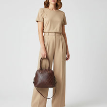 Load image into Gallery viewer, Model carrying the Harley diamond quilted Italian leather dome satchel in dark brown with its crossbody strap
