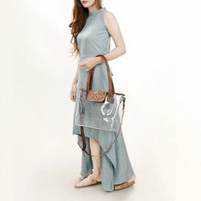 Load image into Gallery viewer, Woman carrying the Acorn Ridge clear stadium tote by its leather top handles, hand tooled oak and acorn flap at front
