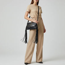 Load image into Gallery viewer, Model wearing the Estrella black studded fringe leather crossbody over the shoulder with tailored neutral trousers
