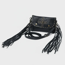 Load image into Gallery viewer, Angled view of the Estrella black studded leather crossbody with fringe falling from both sides and the adjustable strap
