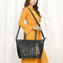 Load image into Gallery viewer, Model wearing the Maple Creek hand tooled leather concealed carry tote in black over the shoulder on its detachable strap
