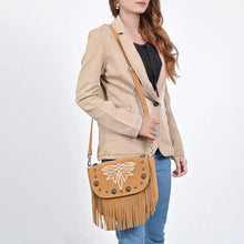 Load image into Gallery viewer, Woman wearing the tan Sparrow suede fringe crossbody purse with a camel blazer and jeans
