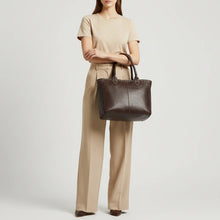 Load image into Gallery viewer, Model carrying the Starla studded leather tote in espresso brown on her forearm, showing its size against a full outfit
