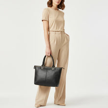 Load image into Gallery viewer, Model holding the Starla studded leather tote in black by its rolled handles, showing its size against a full outfit
