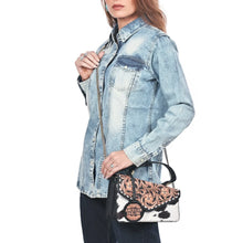 Load image into Gallery viewer, Model carrying the Domino hand-tooled cowhide messenger crossbody on its chain strap with a denim shirt
