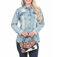 Load image into Gallery viewer, Model holding the Domino tooled cowhide bag by its top handle with a denim shirt and turquoise jewelry
