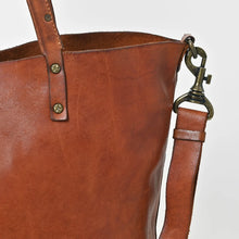 Load image into Gallery viewer, Close-up of the Amber tote showing cognac full-grain leather, brass rivets on the handle and an antique brass swivel strap clip
