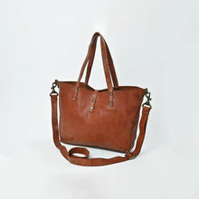Load image into Gallery viewer, Amber riveted leather crossbody tote in cognac, angled view showing the open top, riveted handles and adjustable strap
