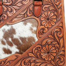 Load image into Gallery viewer, Close-up of the Brazos tote's hand-carved leather, showing the depth of the antique-finished floral and scroll tooling where it meets the hair-on cowhide inset
