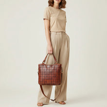 Load image into Gallery viewer, Model carrying the Winslow cognac Italian leather grid tote by its top handles with crossbody strap
