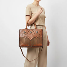 Load image into Gallery viewer, Model carrying the Solstice studded chain fringe leather tote by its top handles with neutral trousers
