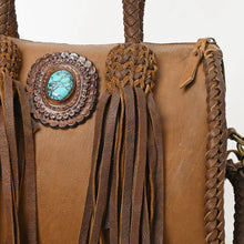 Load image into Gallery viewer, Close-up of the Reata satchel in Caramel: turquoise stone in a hand-tooled rosette, braided fringe tassel, and braided side seam
