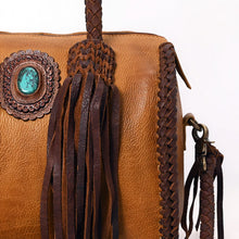 Load image into Gallery viewer, Close-up of the Reata satchel in Honey Tan: turquoise stone in a hand-tooled leather rosette beside braided fringe tassel and braided side seam
