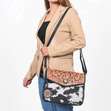 Load image into Gallery viewer, Woman wearing the Magpie black and white cowhide envelope crossbody with tooled sunflower flap
