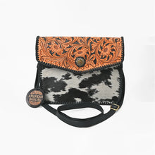 Load image into Gallery viewer, Front view of the Magpie black and white cowhide crossbody with hand tooled leather flap
