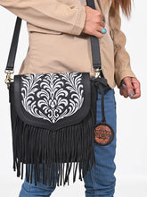Load image into Gallery viewer, Close-up of the Raven fringe crossbody worn on the shoulder, embroidered black leather flap in detail
