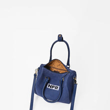 Load image into Gallery viewer, Lockhart navy suede Western speedy bag with NFR embroidered patch and rolled handles. A navy blue suede handbag with a top handle and shoulder strap, featuring a white patch with 'NFR' on the front and a tan patterned lining visible inside, set against a plain white background.
