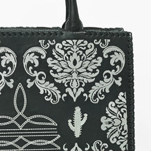Load image into Gallery viewer, Close-up of the Lacey tote's white damask embroidery, boot-stitch detail, embroidered saguaro cactus, and whipstitched leather edge on black pebbled leather
