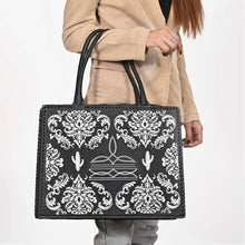 Load image into Gallery viewer, Lacey black leather tote with white damask, boot-stitch, and cactus embroidery held by its rolled handles, worn with a camel blazer
