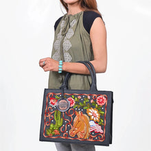 Load image into Gallery viewer, Woman carrying the Liberty black leather tote with colorful horse and American flag embroidery on her forearm, styled with an olive top and turquoise cuff
