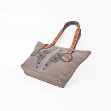 Load image into Gallery viewer, Opal beaded suede tote tilted to show the base with antique brass protective feet and hand-tooled leather straps
