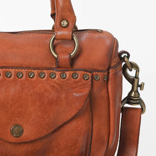 Load image into Gallery viewer, Close-up of the Clementine cognac leather satchel showing star-embossed antique-brass-tone studs, snap-flap pocket, O-ring handle hardware, and swivel snap hook
